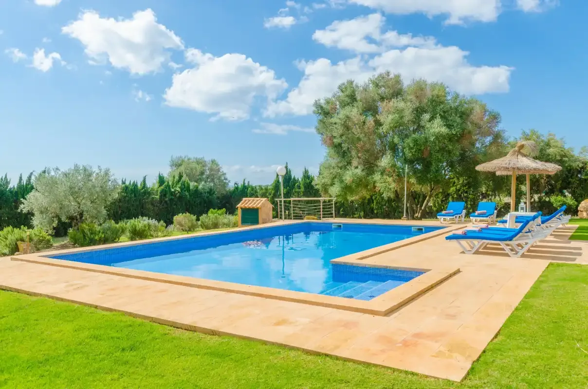 Una piscina al aire libre está rodeada por una terraza pavimentada, tumbonas y césped verde.