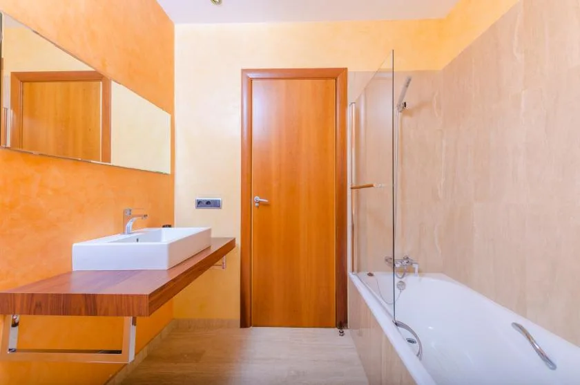 Un baño con bañera, mampara de vidrio y lavabo junto a un tocador de madera.