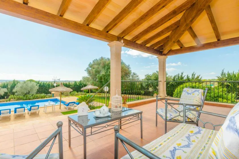 Un patio cubierto al aire libre da a una piscina y un paisaje verde.