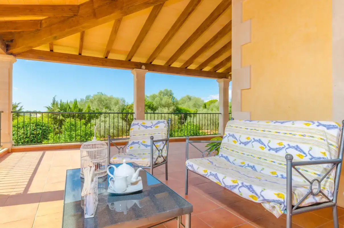 Una terraza cubierta con asientos y una mesa de vidrio da a una zona verde.