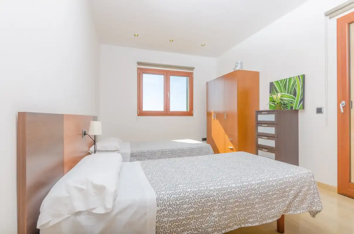 Un dormitorio luminoso con dos camas, una ventana y muebles de madera.