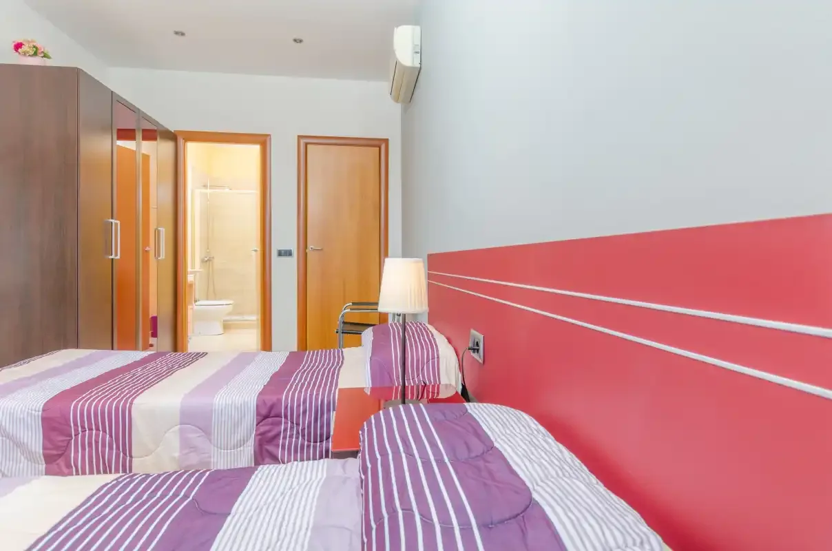 Dormitorio con ropa de cama a rayas, armarios y una pared roja.