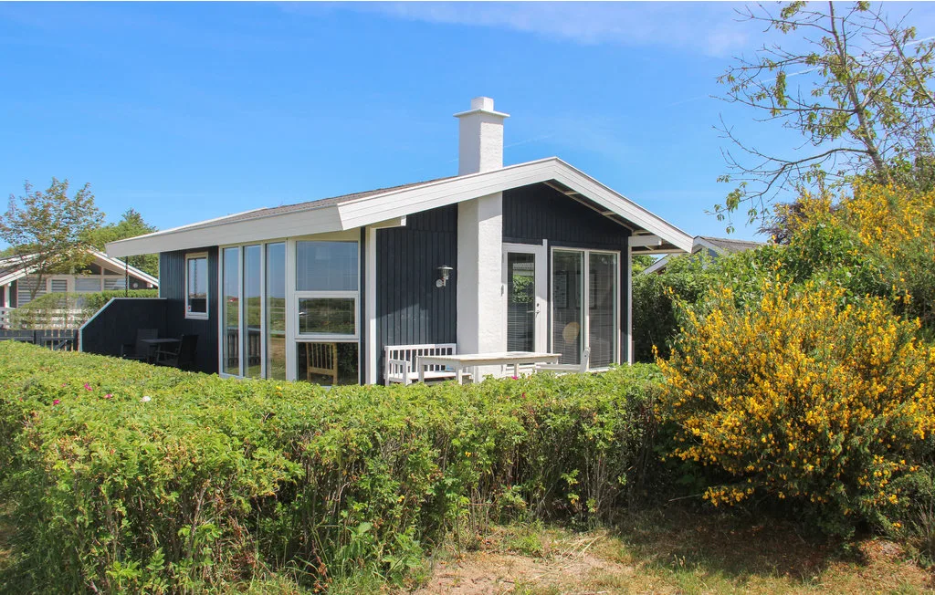 A modern house sits behind a hedge, with large windows and a sloped roof.