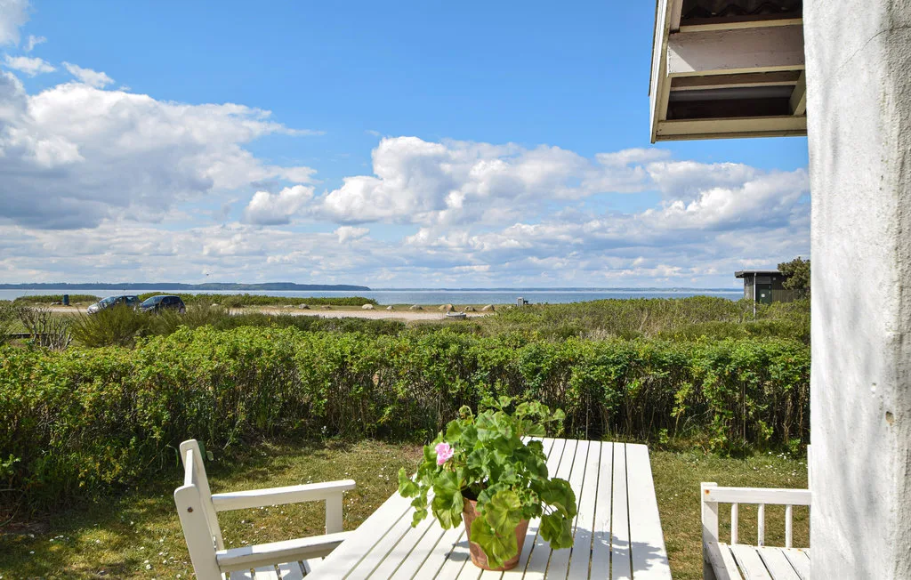 An outdoor seating area overlooks a hedge and the water beneath a partly cloudy sky.