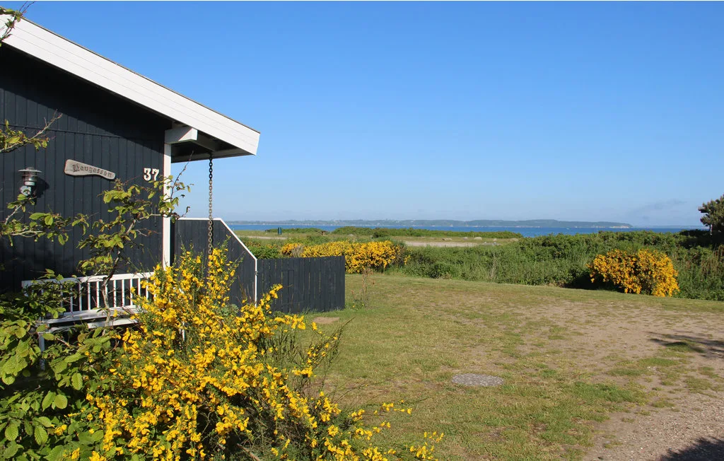 A dark-sided building stands beside a grassy yard with a distant water view.