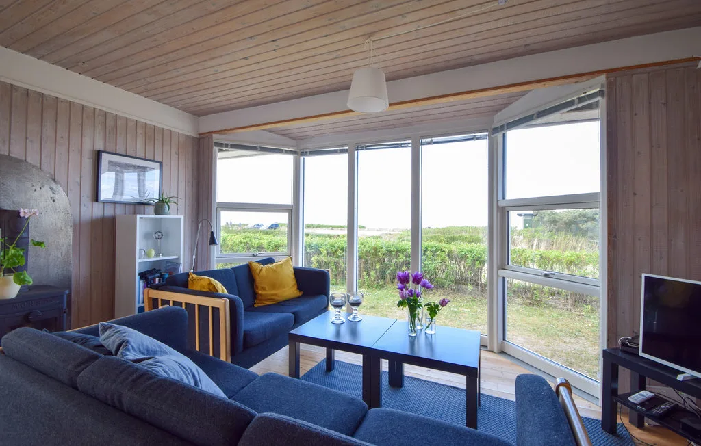 Una sala de estar con asientos azules y grandes ventanas con vistas a la vegetación.