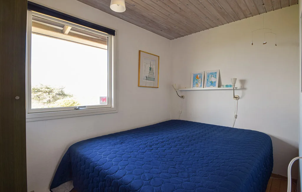 A bedroom with a bed covered in a blue quilt beside a large window.