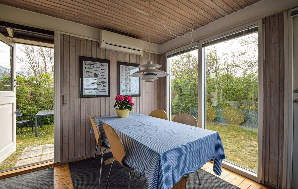 A dining area with a long table beside large windows overlooking greenery.