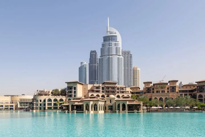 Un horizonte urbano se alza tras un paseo junto al agua turquesa.