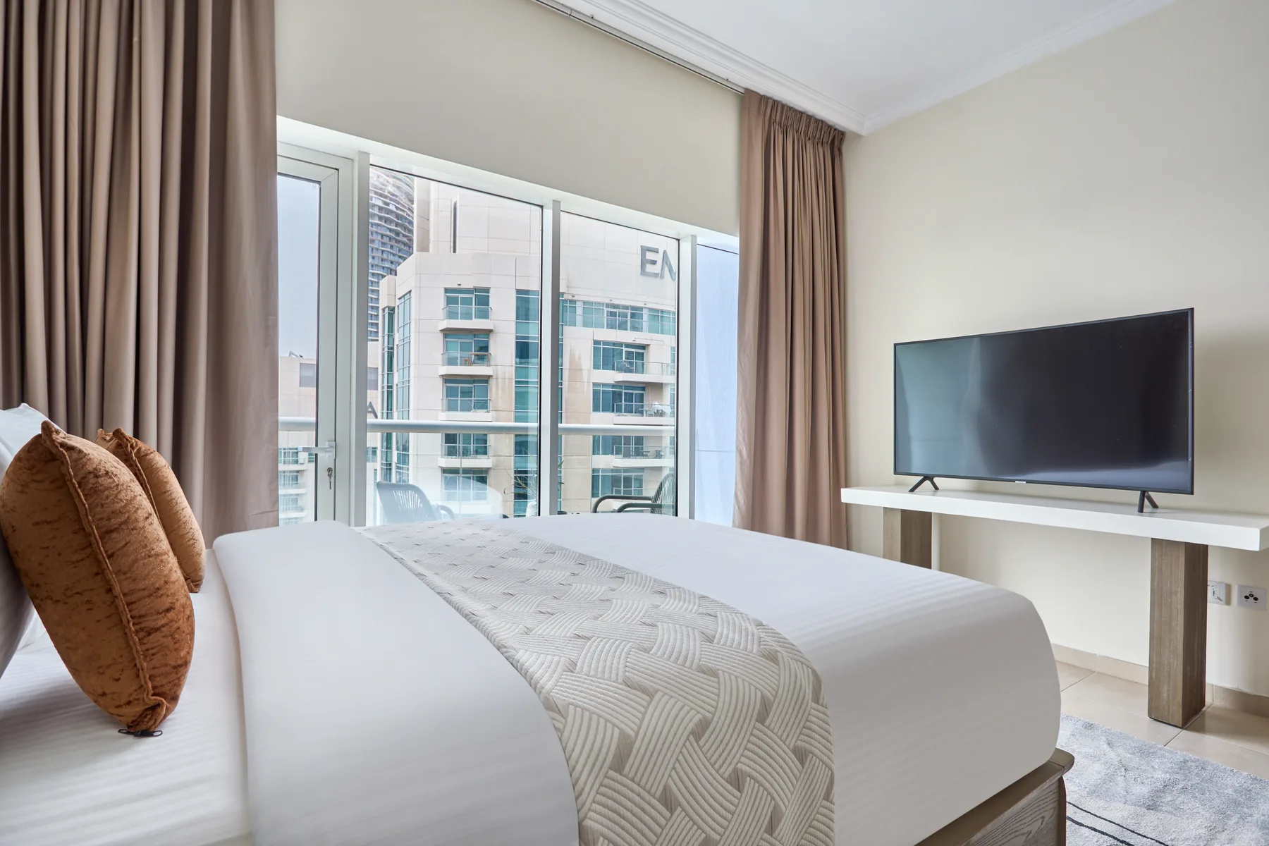 Un dormitorio con una cama bien tendida y un televisor junto a una ventana grande.