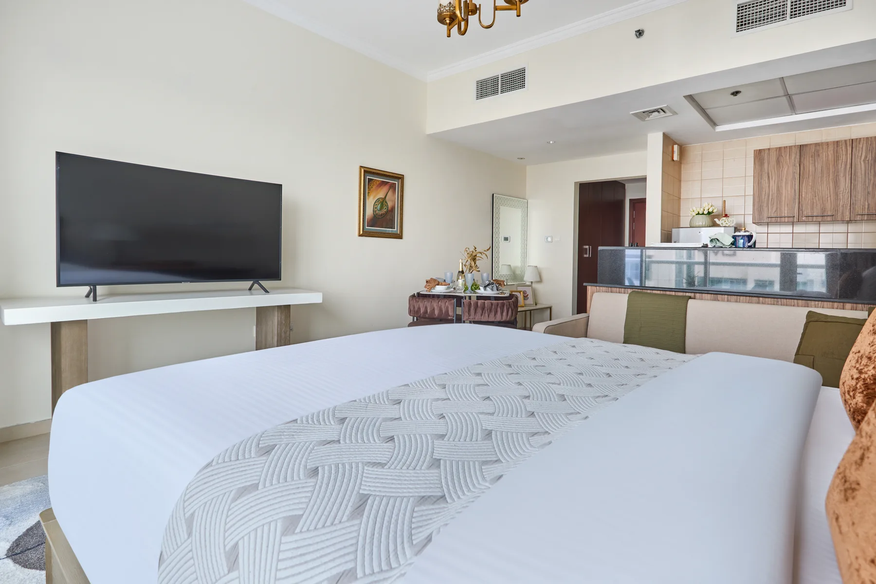 Dormitorio con una cama grande, un televisor y una cocina pequeña al fondo.