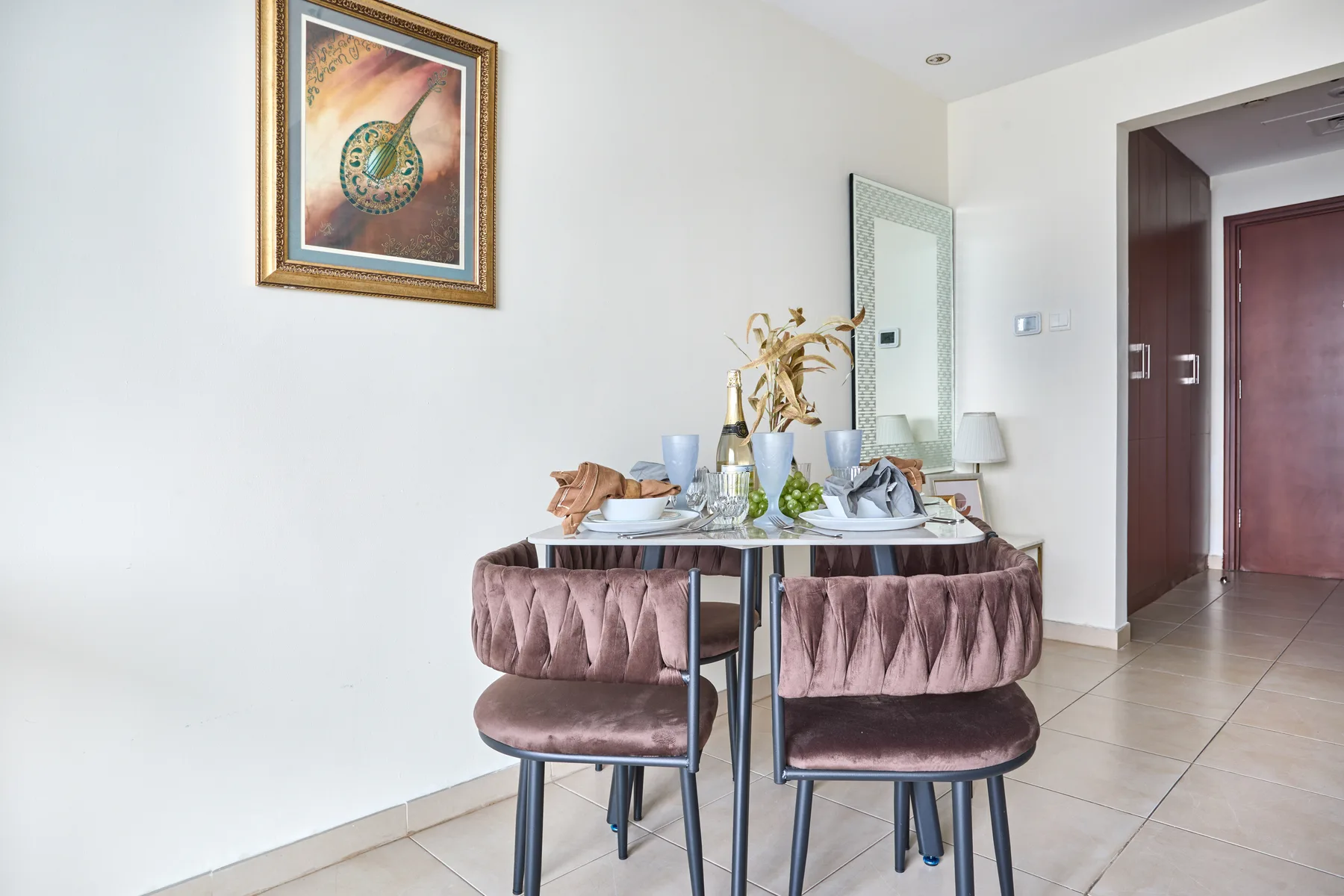 Comedor con una mesa puesta, asientos tapizados y una obra enmarcada.