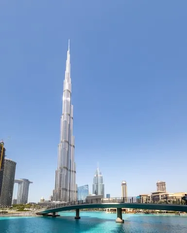 El Burj Khalifa se eleva sobre una piscina azul y un puente peatonal curvo.