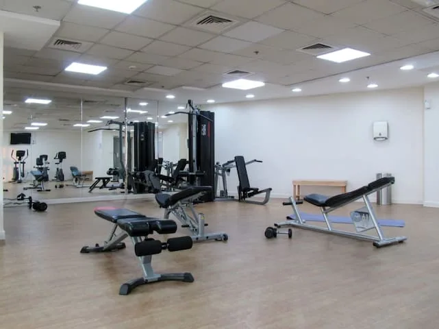 Un gimnasio con máquinas de pesas, bancos y una pared con espejos.