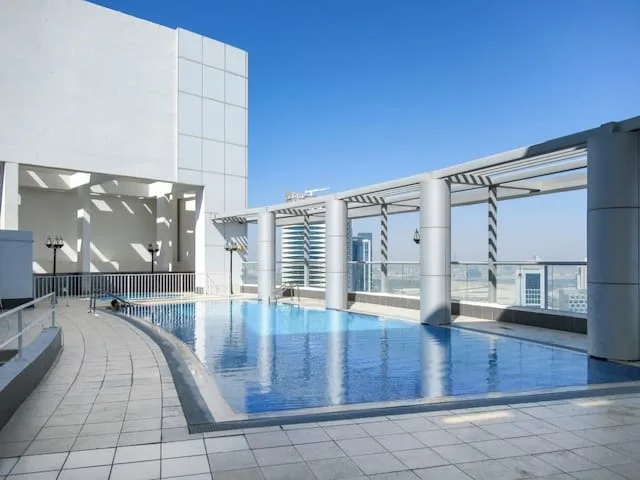 Una piscina en la azotea junto a una terraza pavimentada y un edificio blanco moderno.