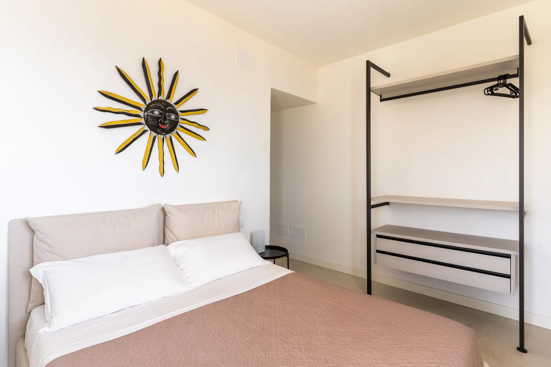 Un dormitorio con una cama, almohadas blancas y un perchero abierto.