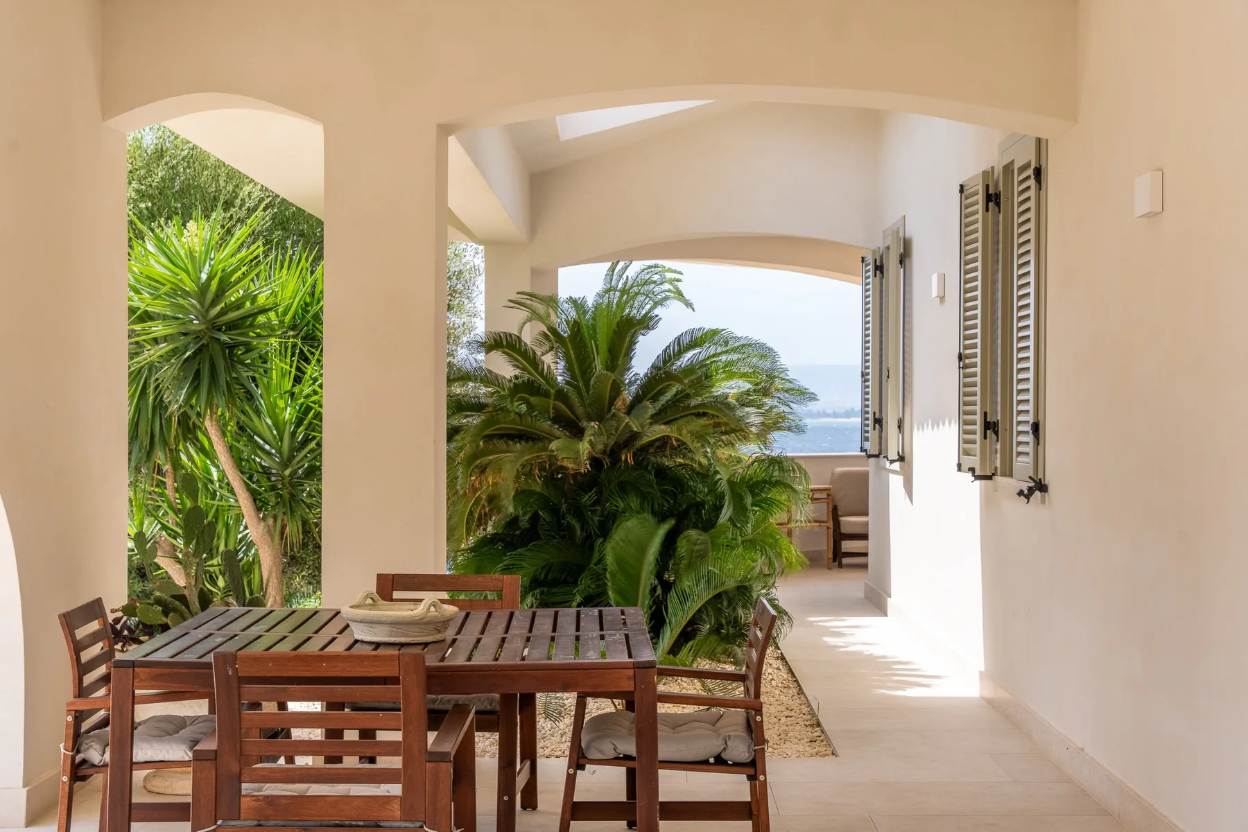 Un comedor exterior soleado se abre a un jardín frondoso.