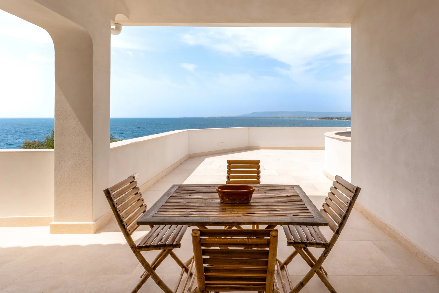 Una terraza cubierta con una mesa de comedor de madera y asientos frente al mar.