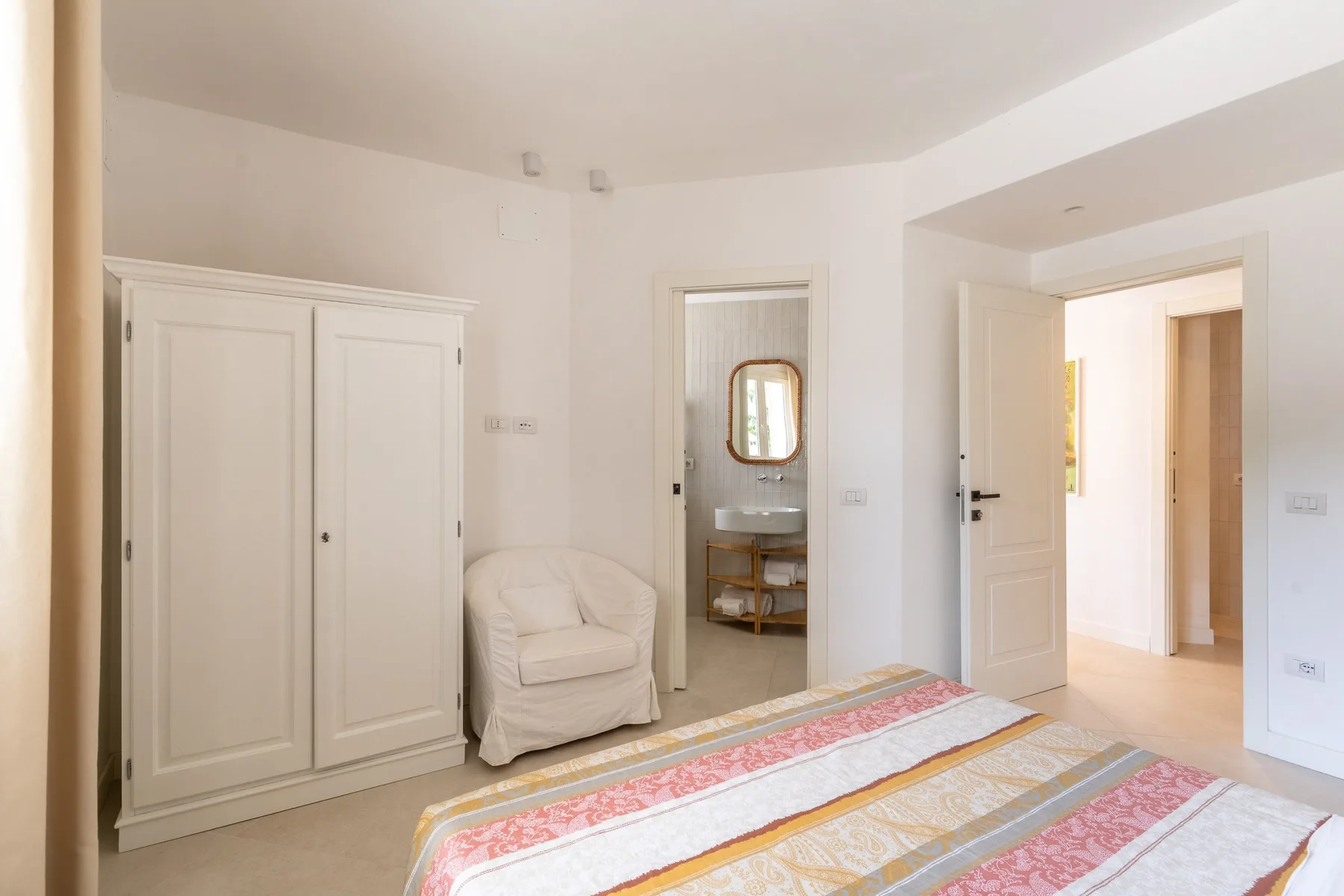 Un dormitorio luminoso con una cama, un armario y una puerta abierta.