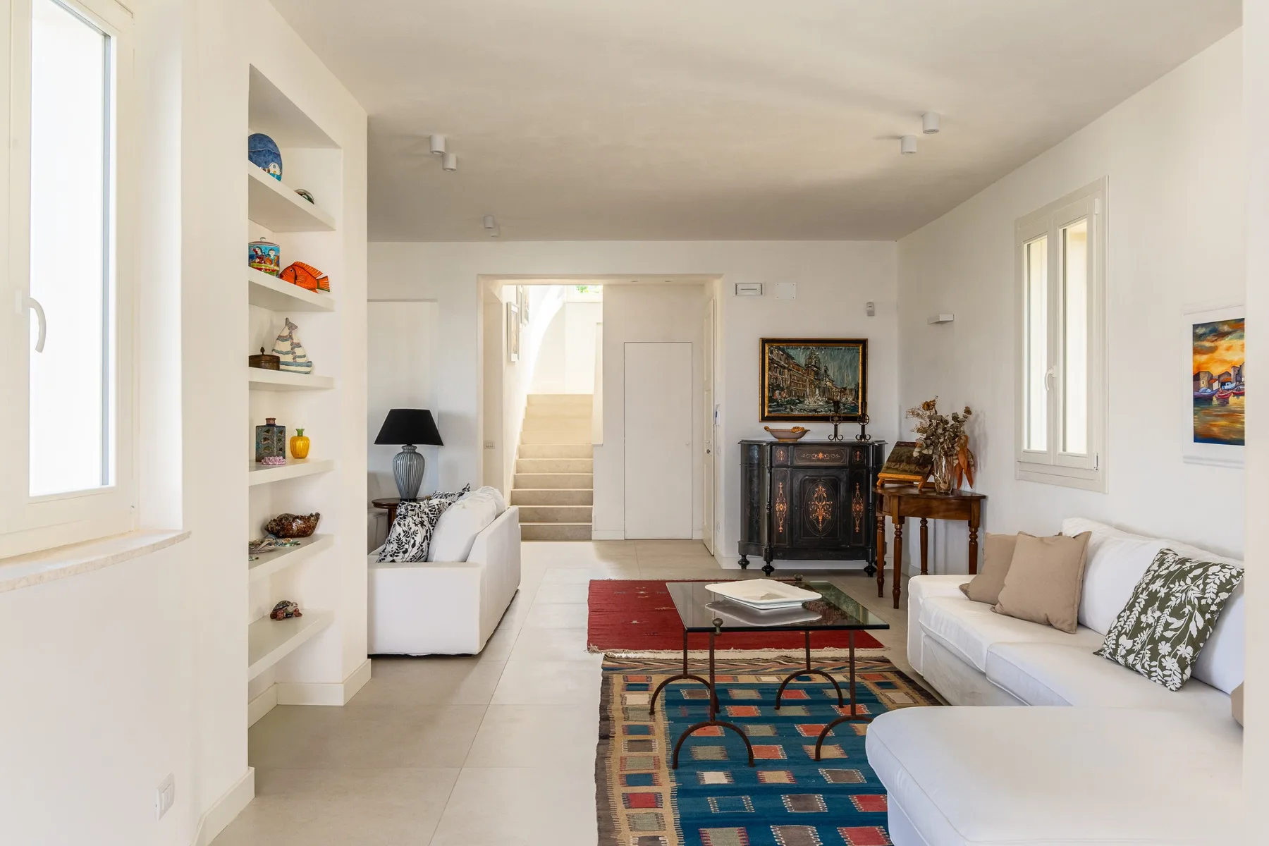 Una sala luminosa con asientos blancos, estantes empotrados y una alfombra estampada.