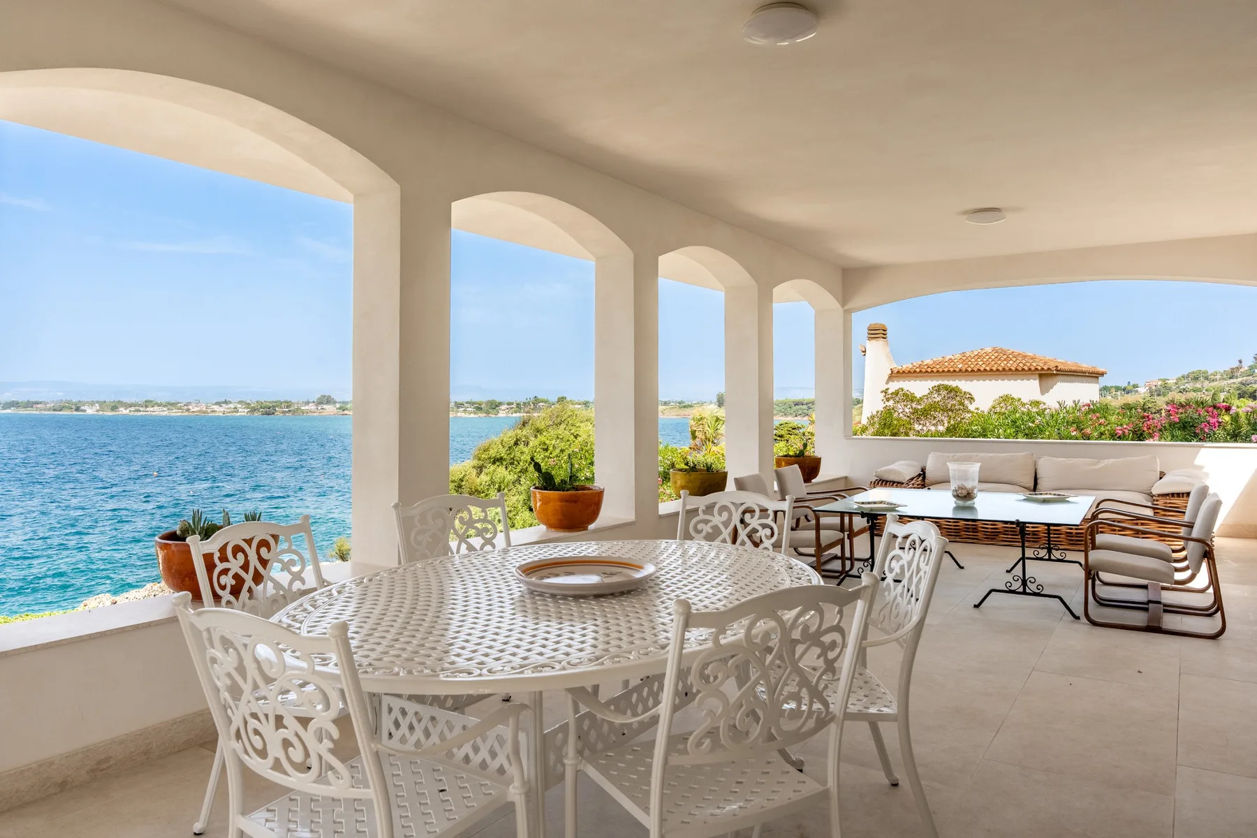 Una terraza cubierta junto al mar, con muebles blancos y vistas al agua.