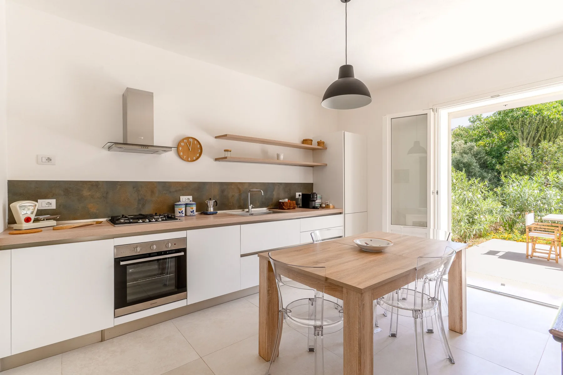 Una cocina luminosa con comedor y una mesa de madera junto a las puertas abiertas al patio.