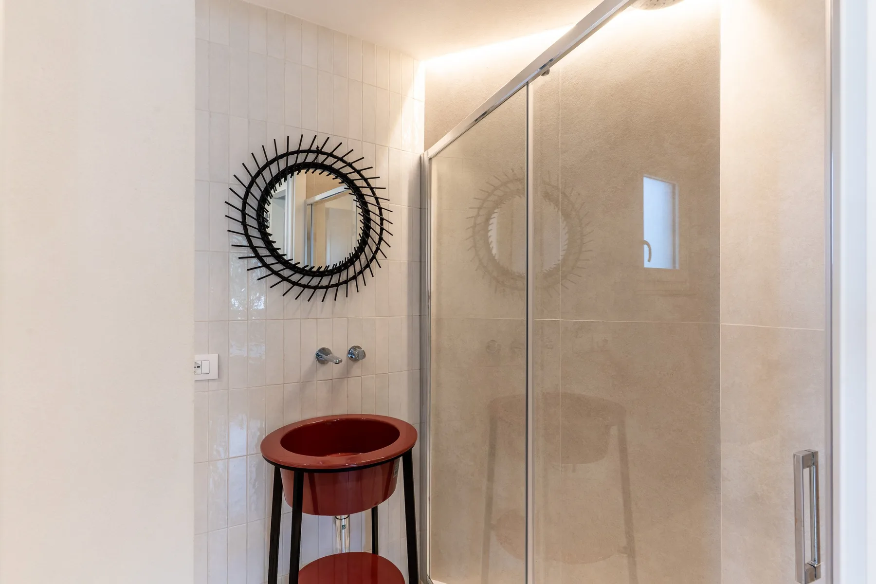 Un baño con azulejos, una ducha de vidrio y un espejo redondo en la pared.