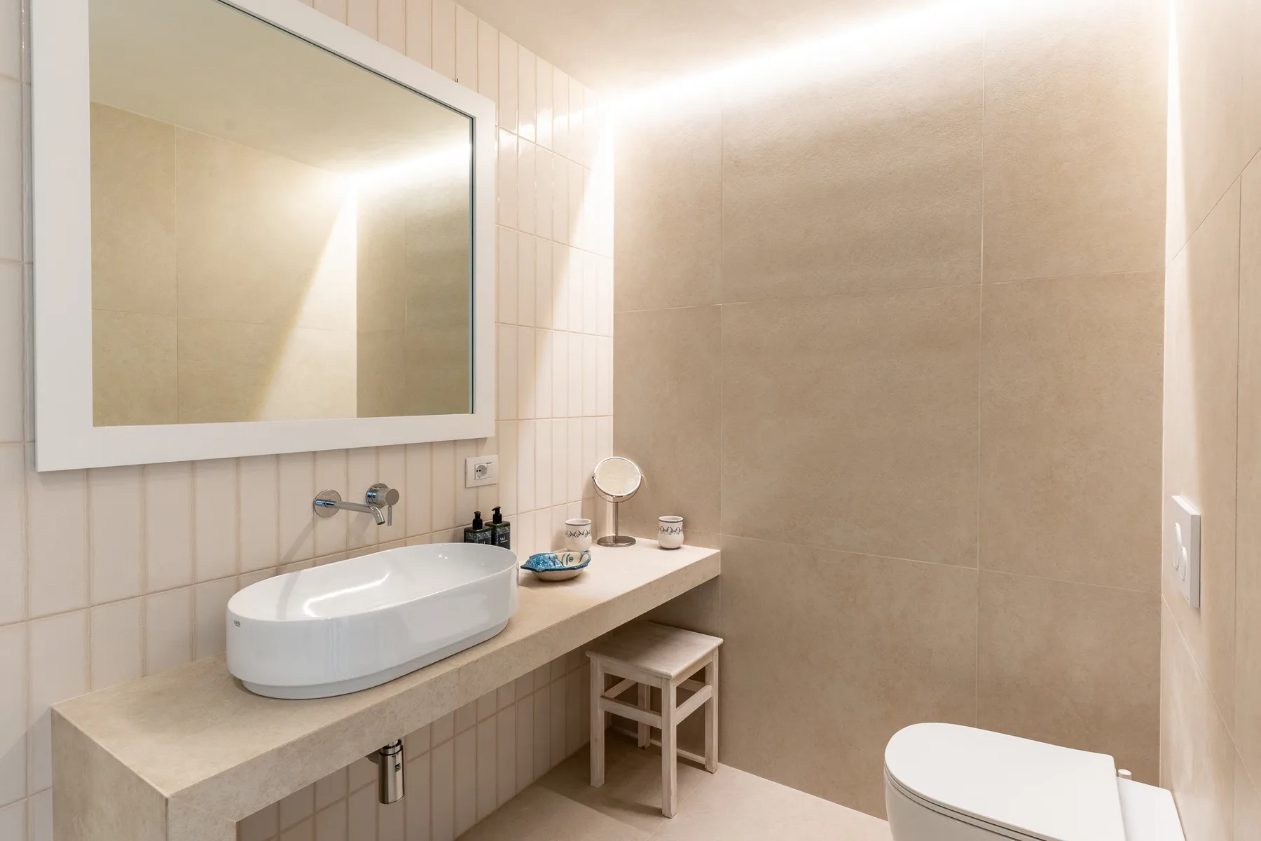 Un baño alicatado con lavabo sobre encimera, espejo grande e inodoro.