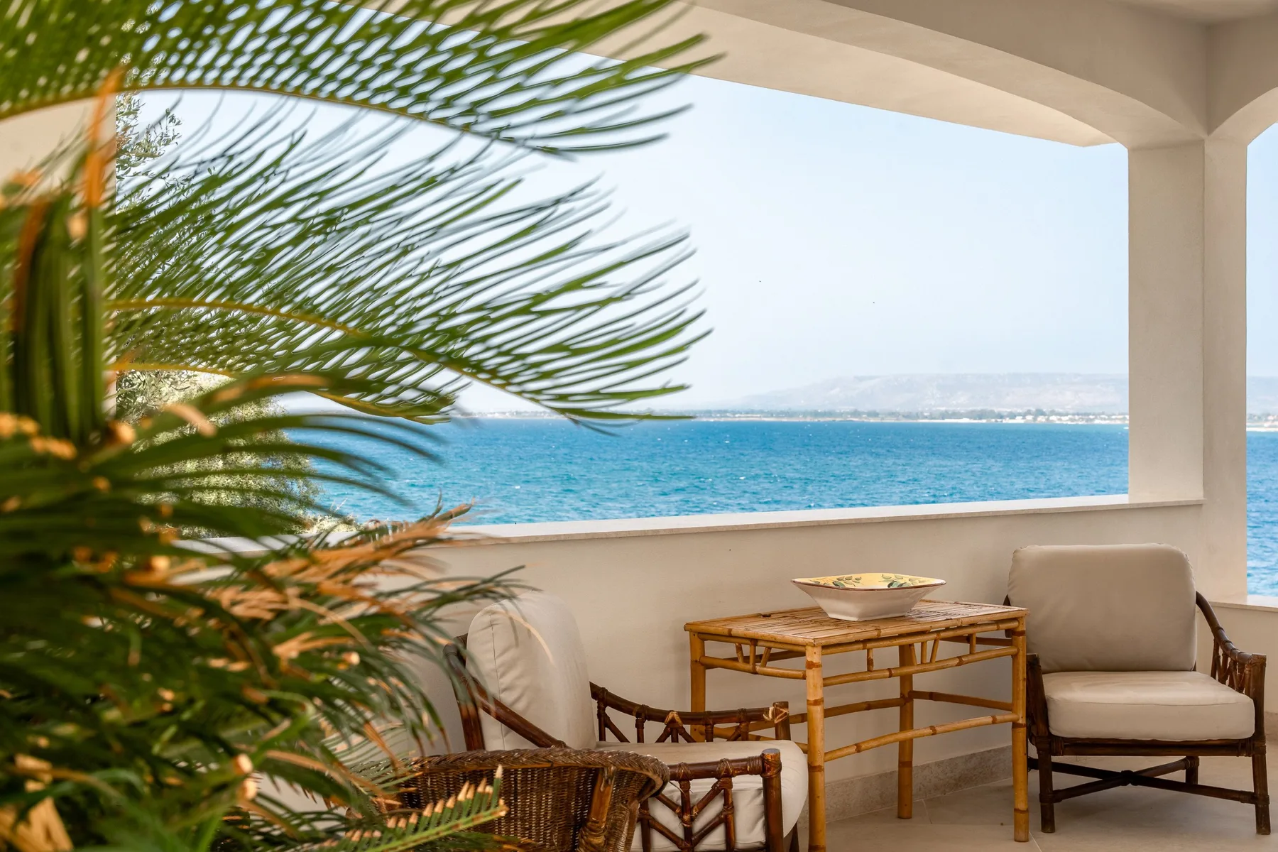 Una terraza cubierta da al mar, con asientos y una mesa pequeña.