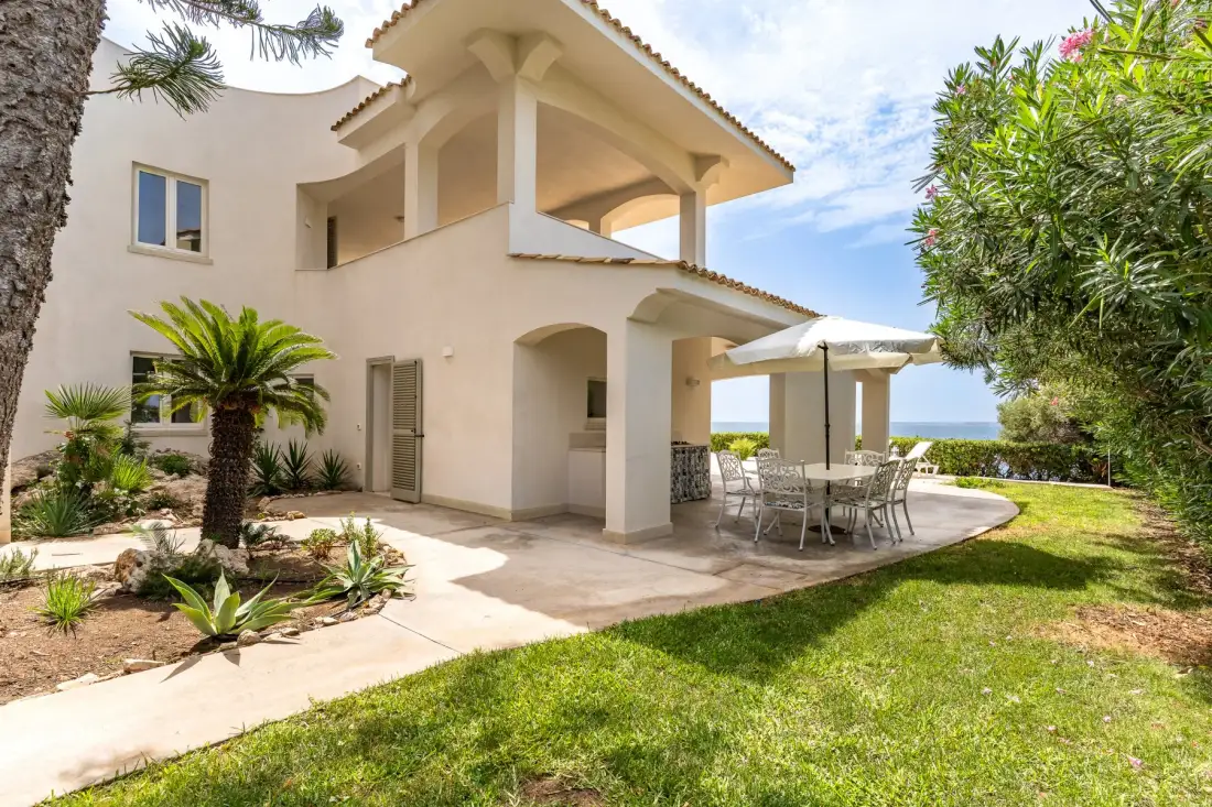 Una casa blanca de dos plantas con un patio sombreado y una zona de comedor al aire libre.
