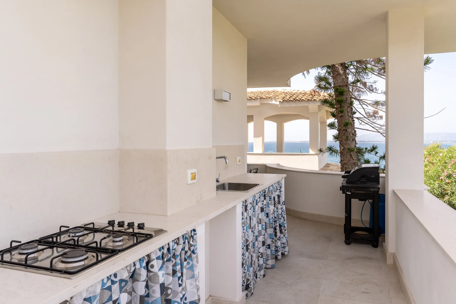 Una cocina exterior cubierta con una placa de gas y vistas al mar.