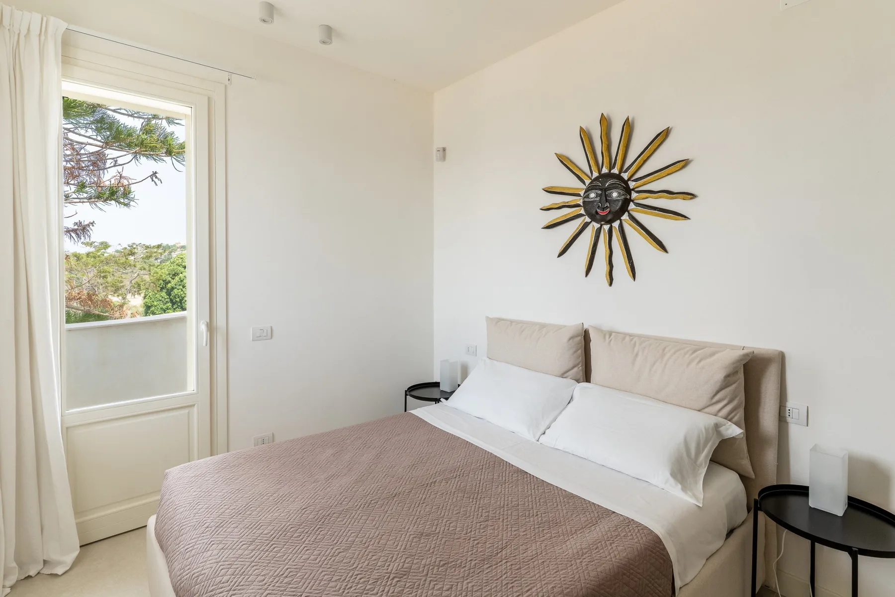 Un dormitorio luminoso con una cama bien arreglada y un adorno de pared en forma de sol.