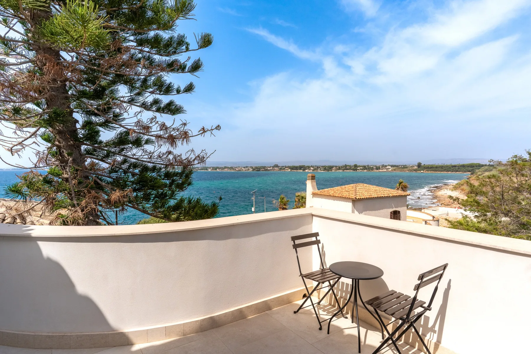 Una terraza en la azotea mira al mar, con una mesa pequeña y asientos.