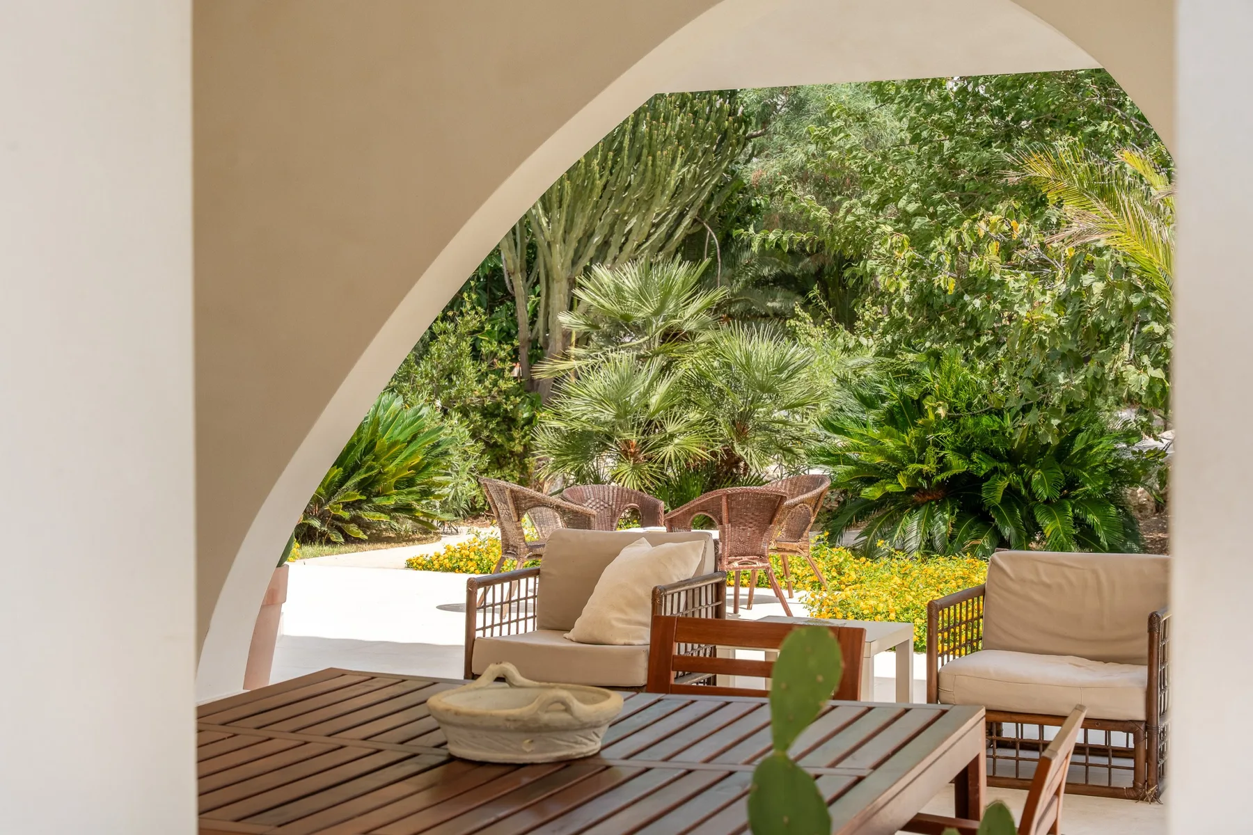 Un patio sombreado con asientos de madera da a un jardín frondoso.