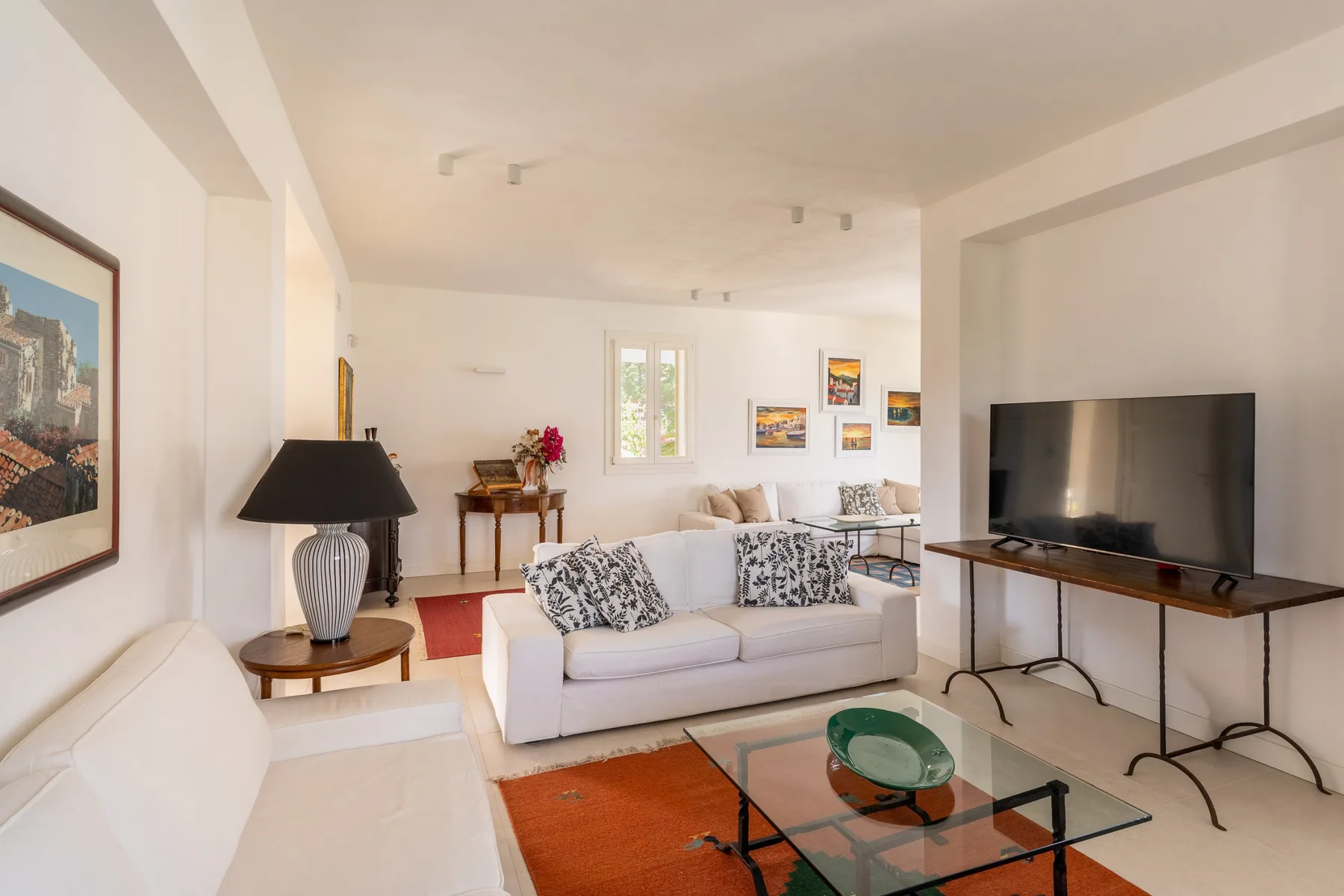 Una sala luminosa con asientos, una mesa de centro de vidrio y un televisor.