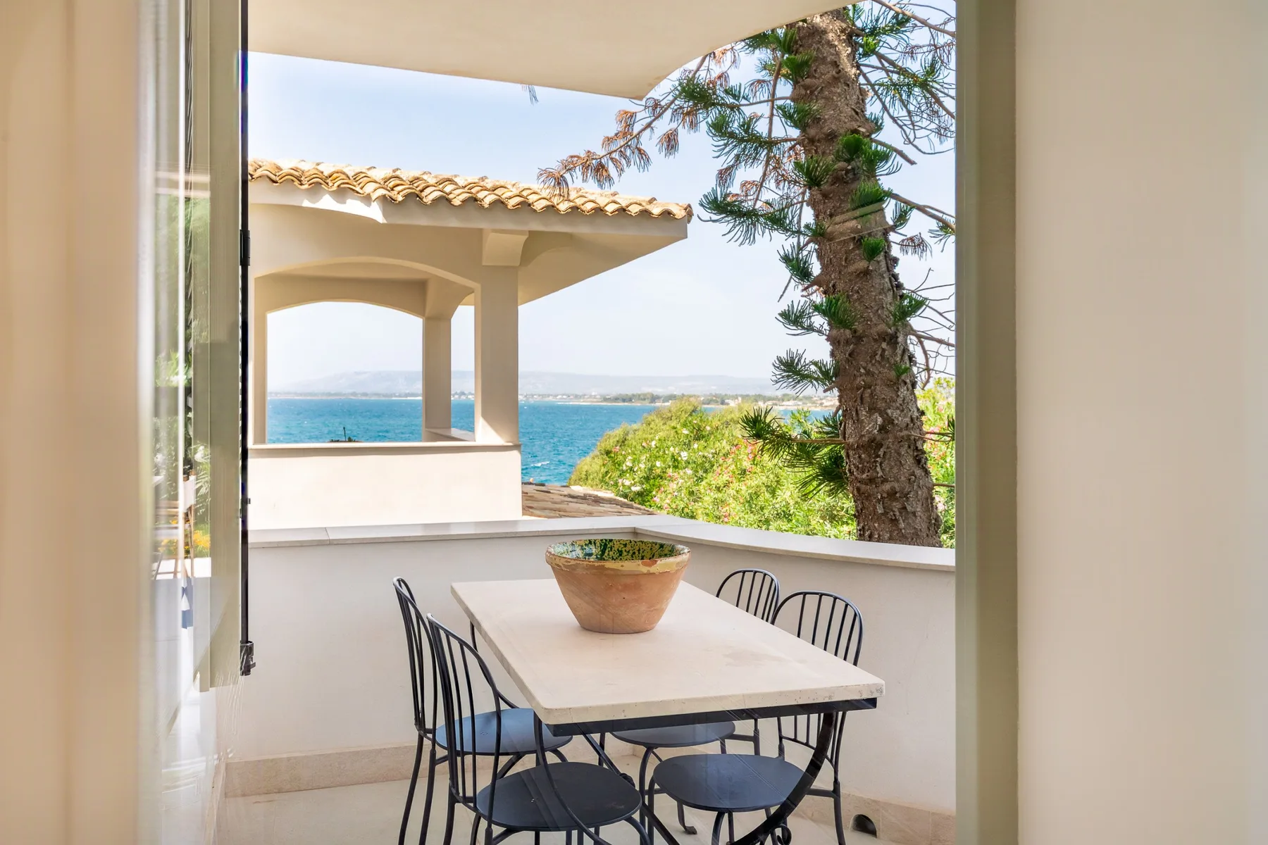 Una zona de comedor en una terraza cubierta da al mar, con mesa y asientos.