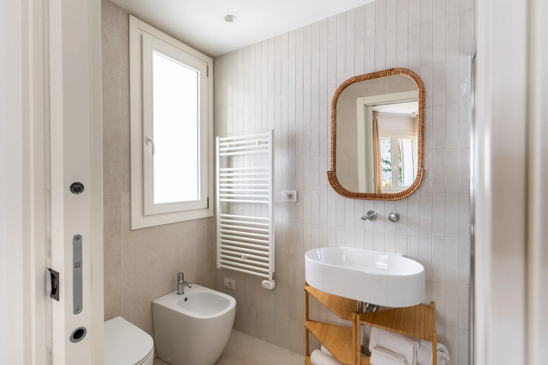 Un baño luminoso con lavabo, bidé y toallero calefactable de pared.