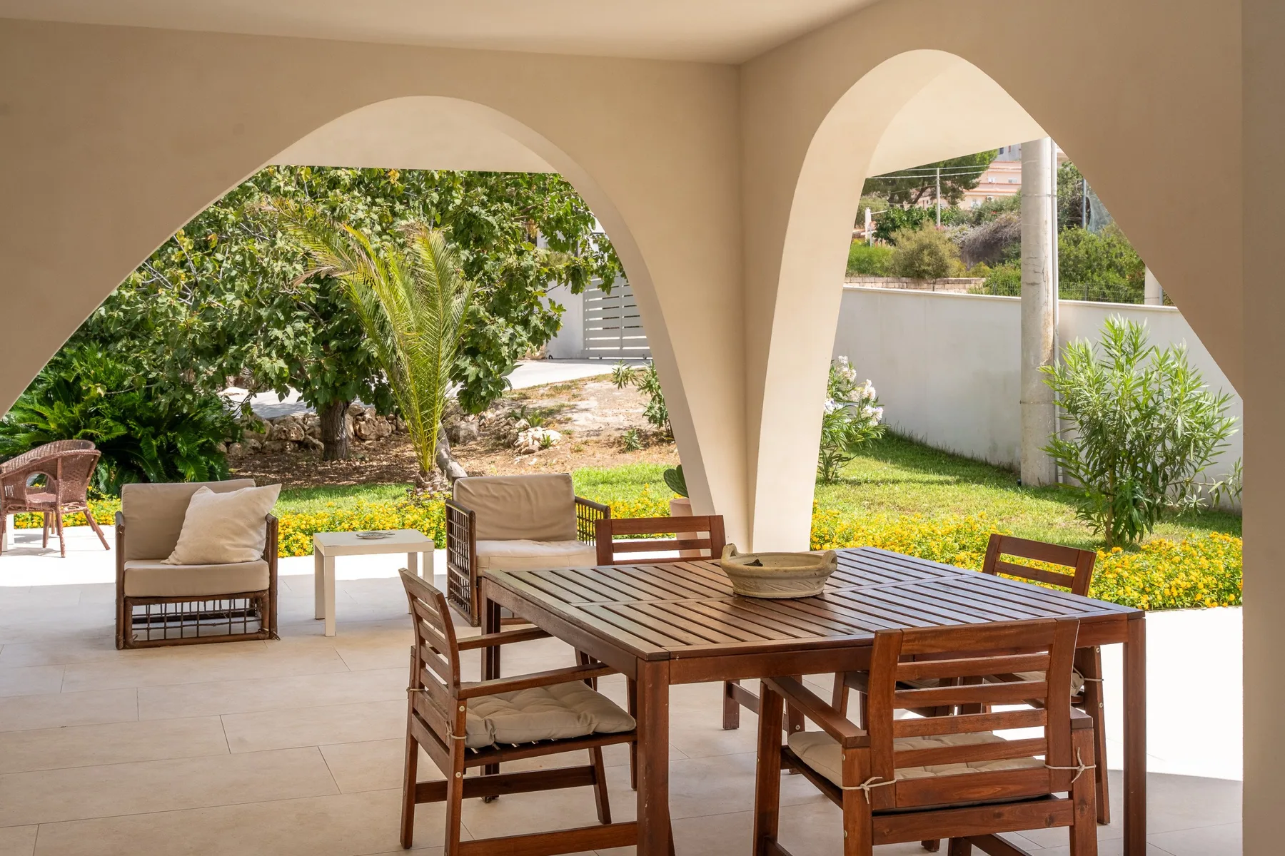 Un patio cubierto con una mesa de comedor de madera y sillas frente a un jardín.