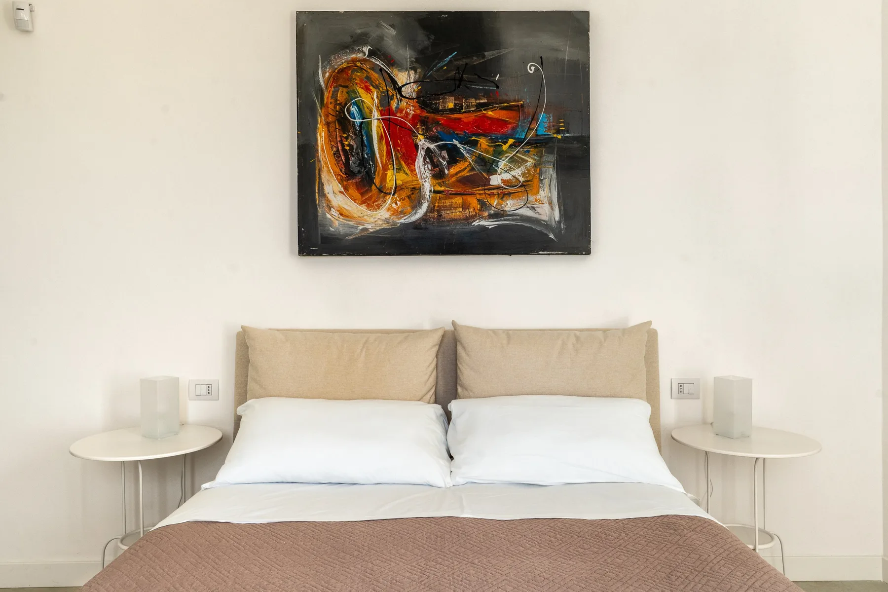 Un dormitorio con una cama doble bajo una pintura abstracta.
