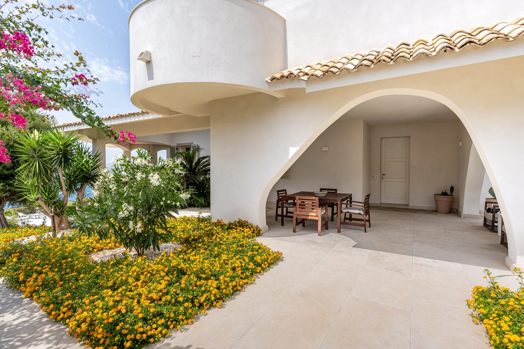 Un patio de estuco blanco con un arco, asientos al aire libre y plantas con flores.