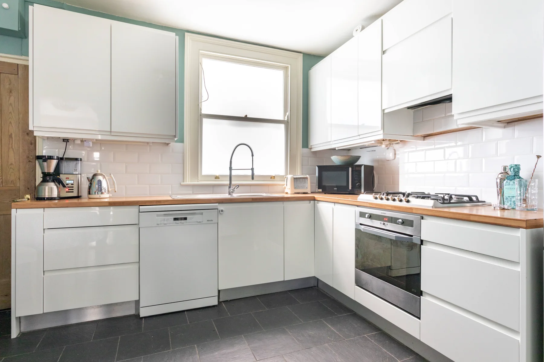 A bright kitchen with white cabinets, tiled walls, and a central window.