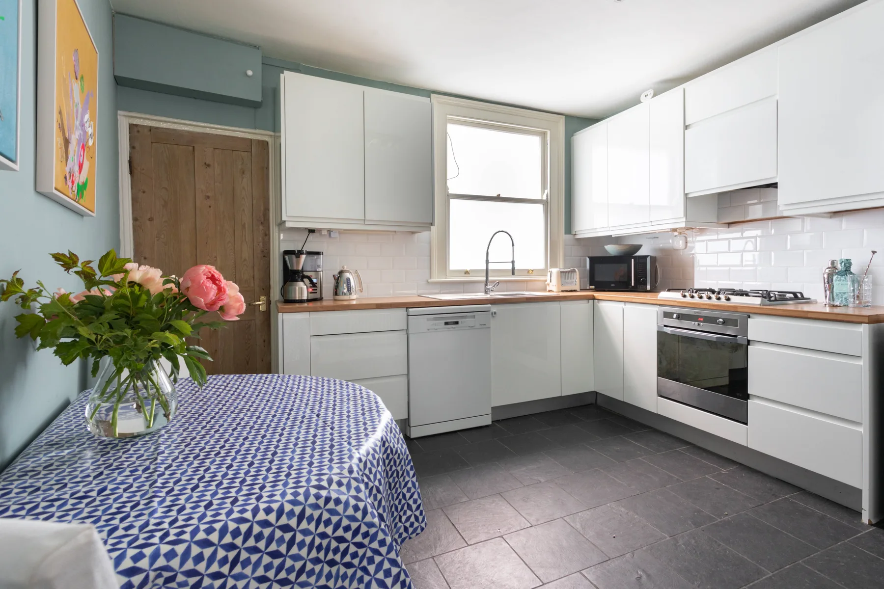 A bright kitchen with white cabinets, a window, and a dining table.
