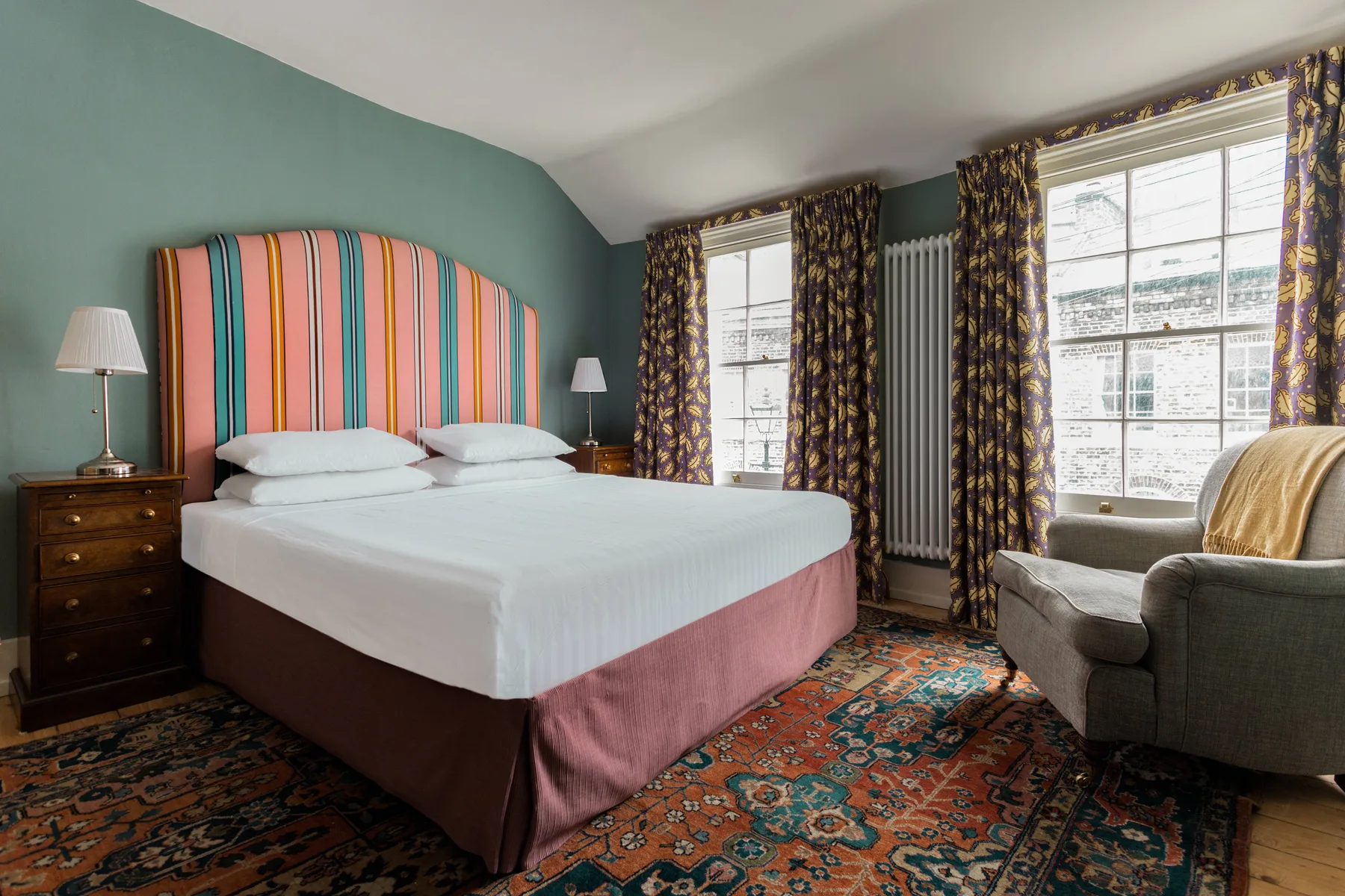 A bedroom with a large bed, patterned rug, and tall windows.