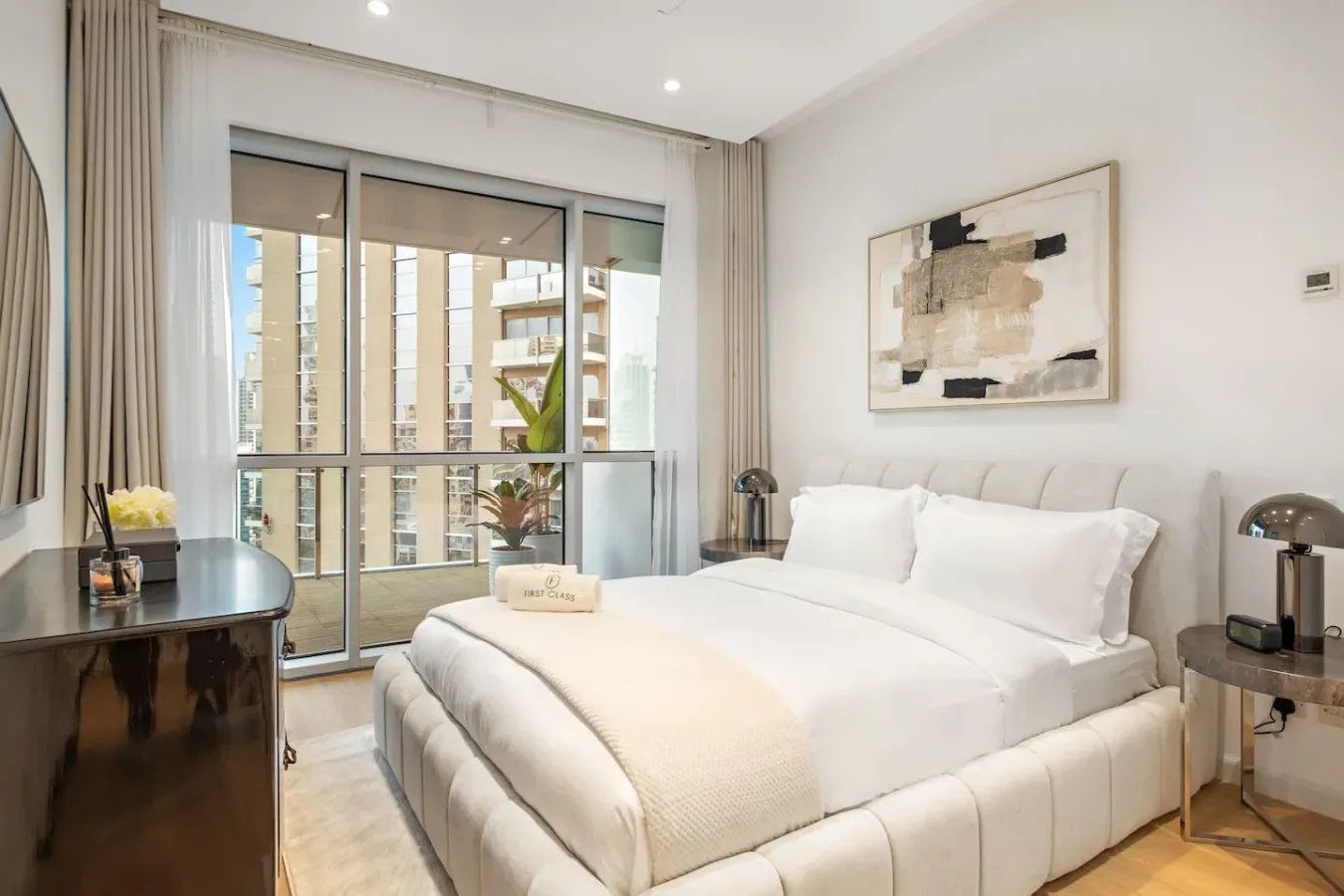 Un dormitorio luminoso con una cama tendida junto a grandes ventanas.