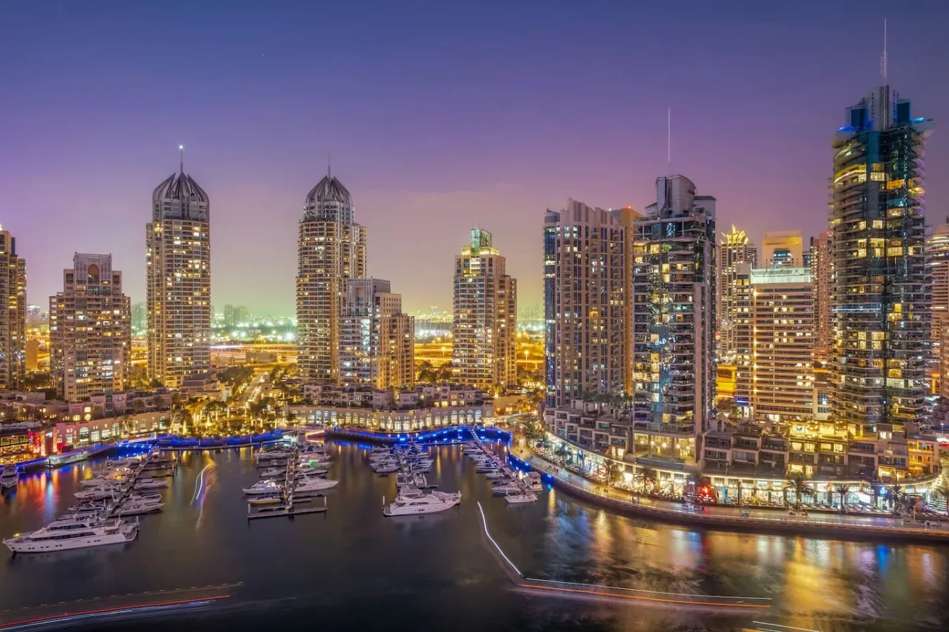 Un horizonte urbano nocturno se alza sobre una marina llena de embarcaciones.
