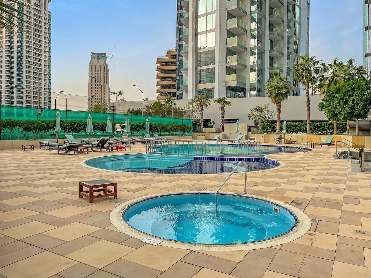 Una zona de piscina al aire libre con una piscina circular más pequeña en primer plano y asientos cerca.