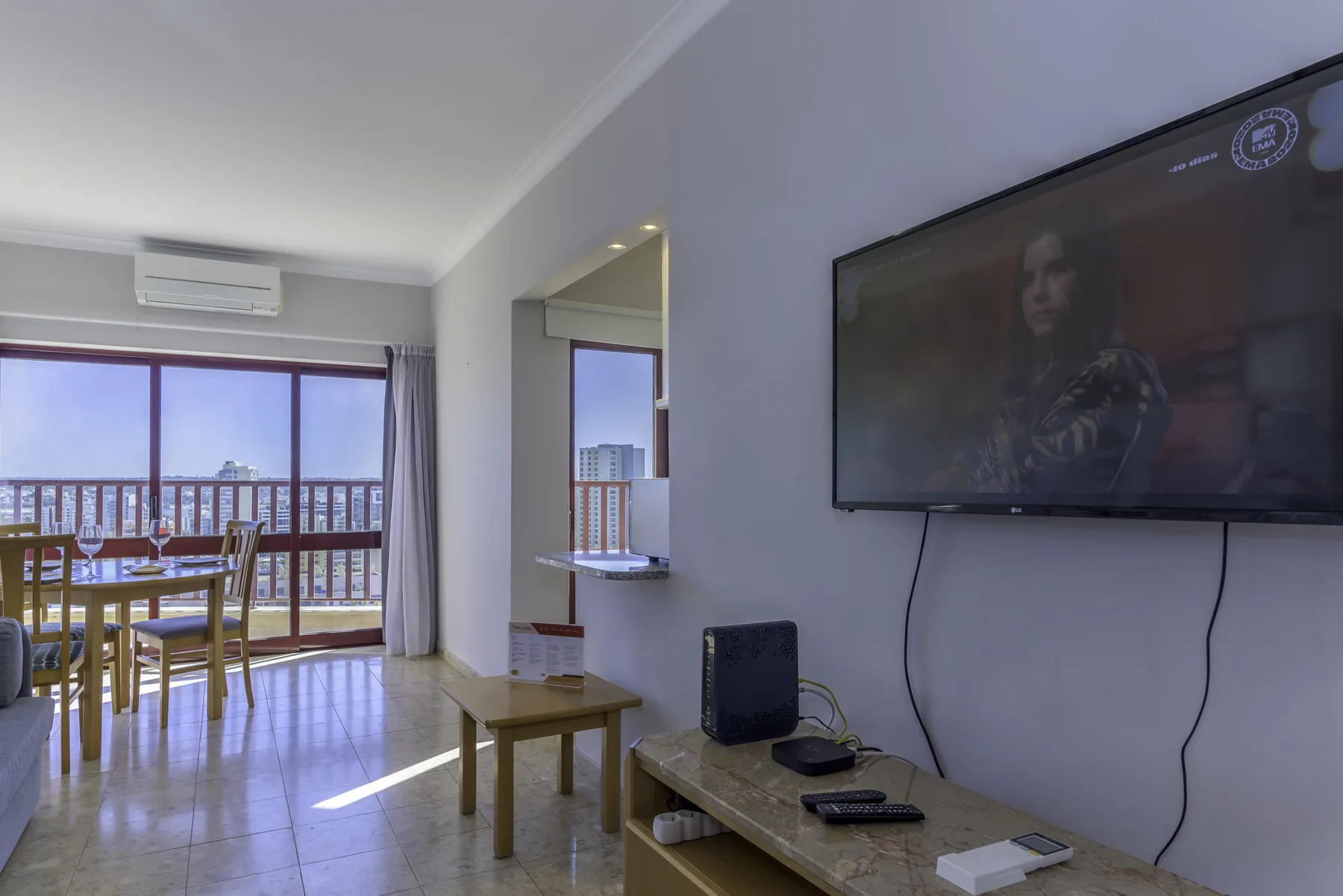 A living room with a television, seating, and a dining area beside a balcony.