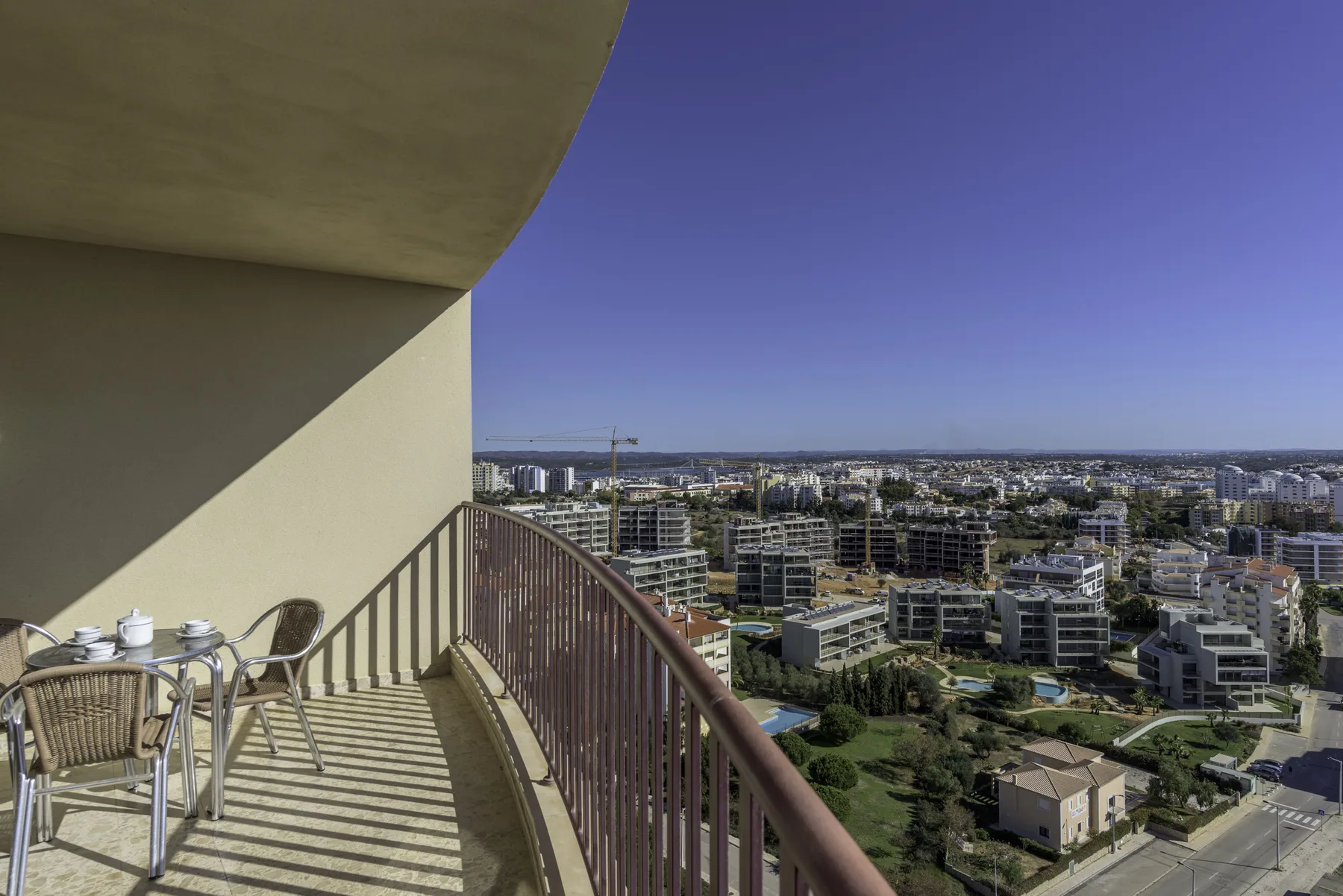 A balcony with outdoor seating overlooks a cityscape under a clear sky.