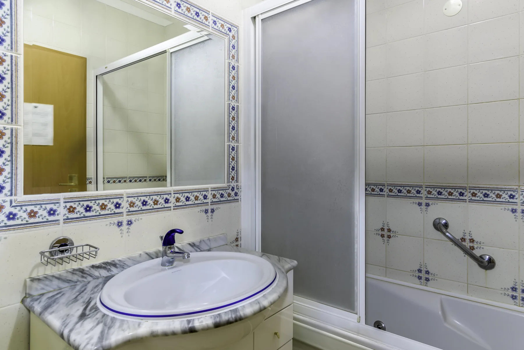 A tiled bathroom with a sink, mirror, and bathtub.