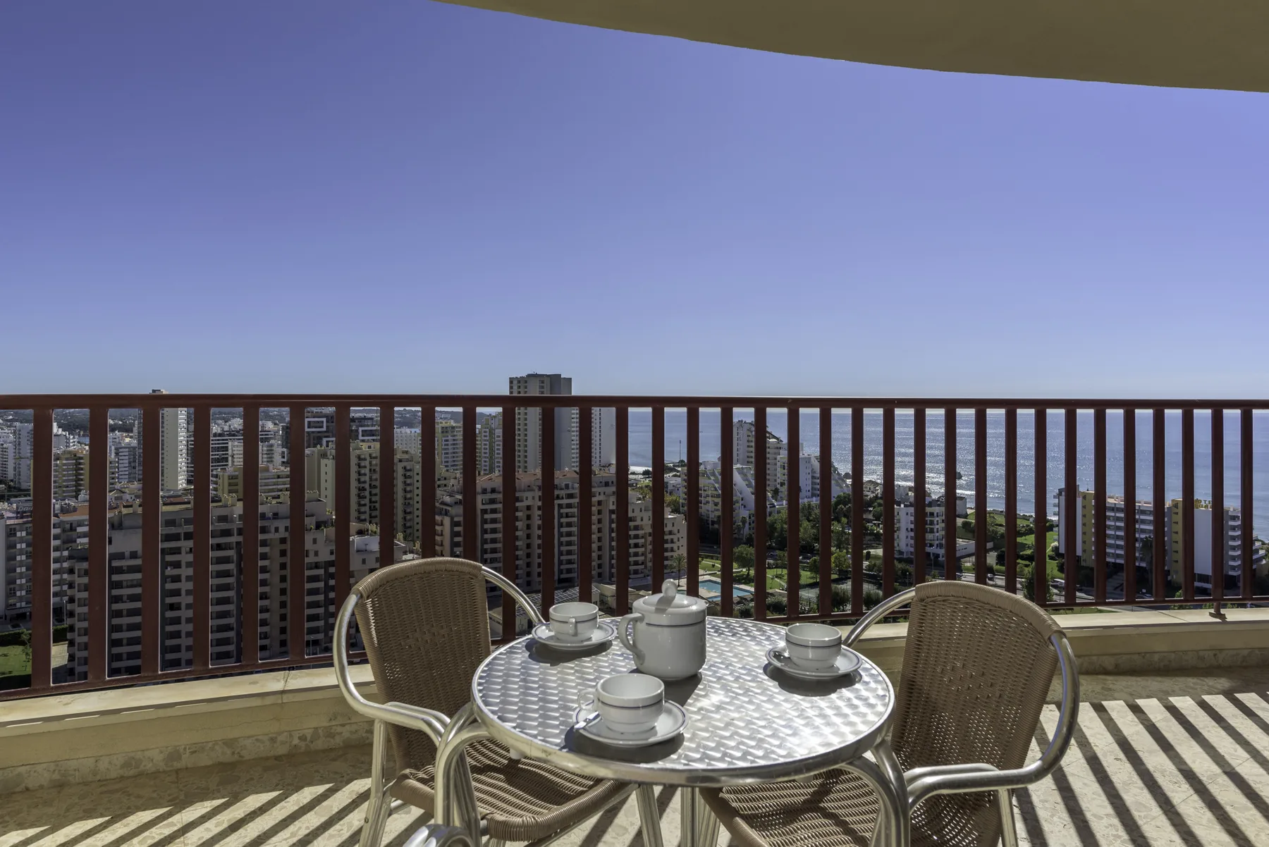 A balcony seating area with a round table overlooks nearby buildings and the water.